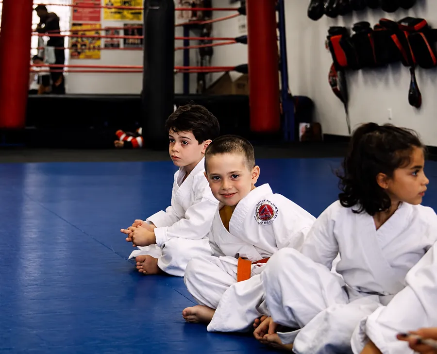 Dean as a young boy in a white gi with an orange belt, sitting on the mats in a martial arts class