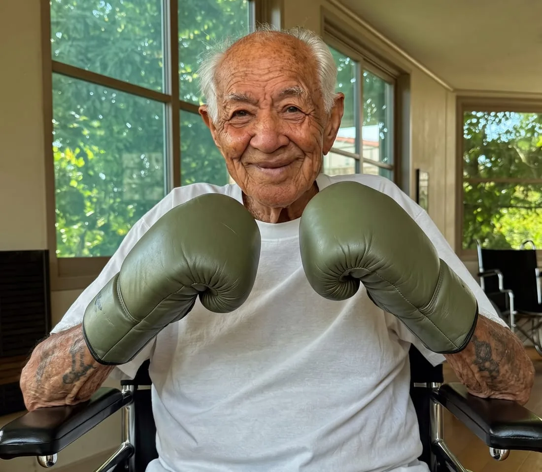 An older man in a wheelchair grinning with boxing gloves raised — the fighter every corner works for